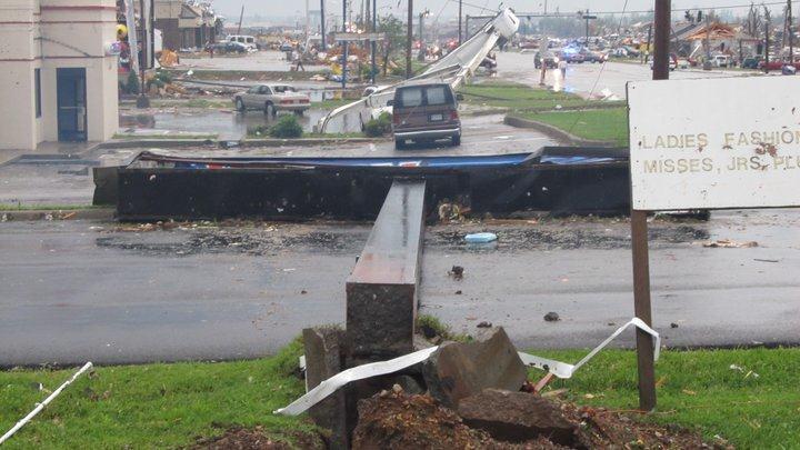 Large signs have been pushed over, additional damage to buildings visible in background.